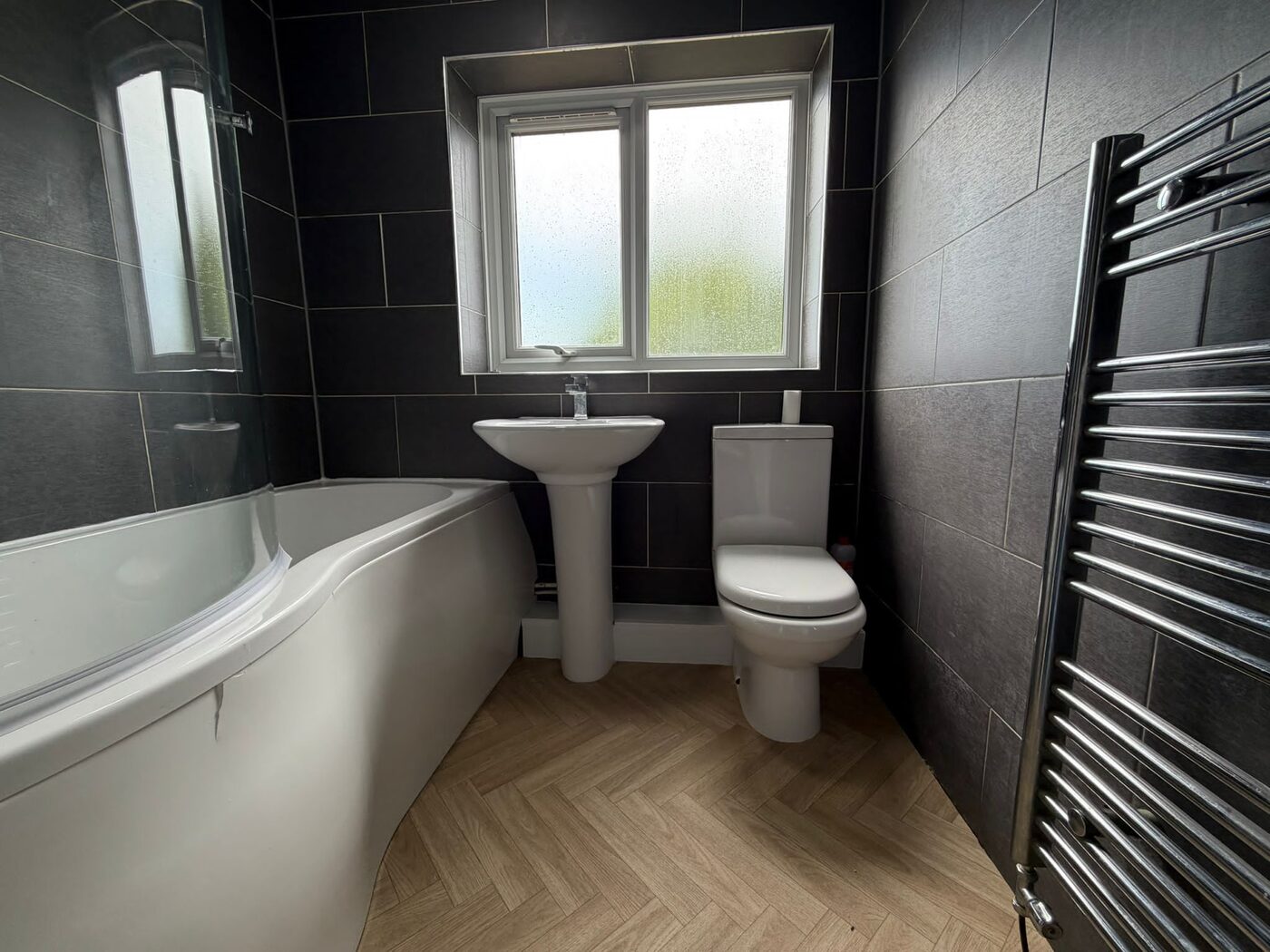 Refurbished bathroom with dark tiling and towel radiator